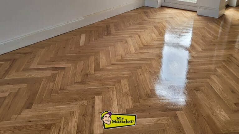 A beautifully restored herringbone parquet floor with a high-gloss polished finish, showcasing expert craftsmanship.