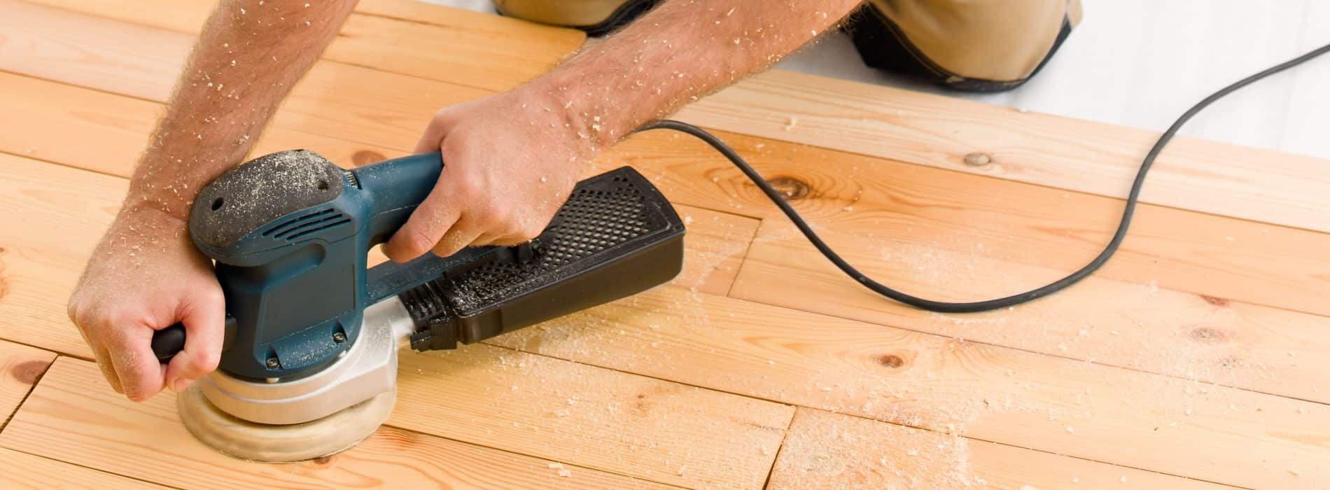 A Mr Sander® in Kingston skilfully uses a 240v wired Makita Orbital Sander, equipped with a 125mm finest grit sanding disc, to effectively remove previous scratches and imperfections on a wooden floor, ensuring a smooth finish.