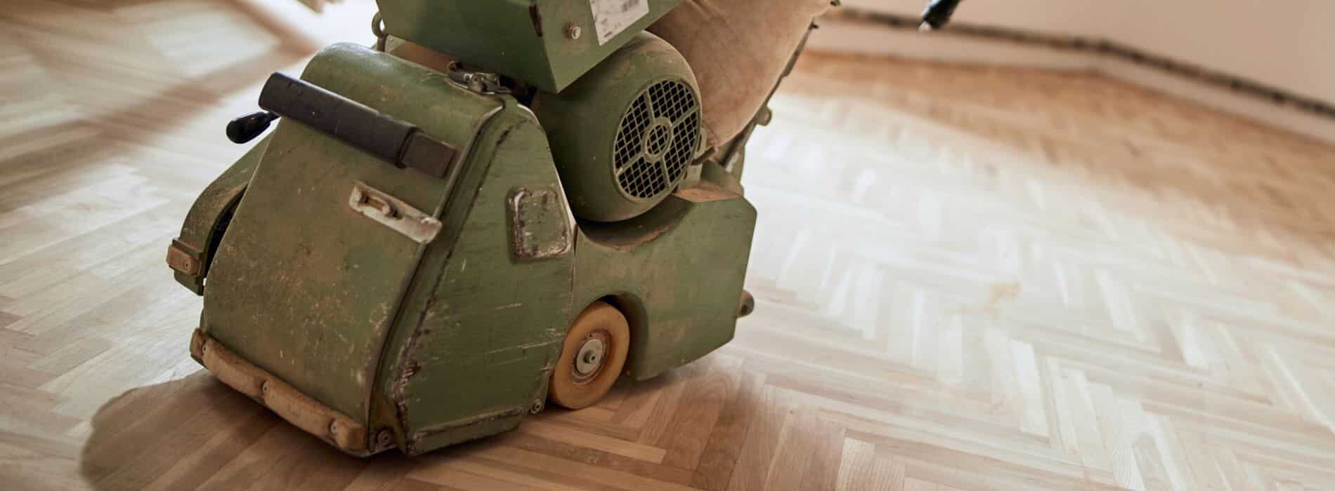 A green Lagler 200mm x 750mm sanding machine sits on top of a stunning hardwood floor, ready to transform it to its former glory.