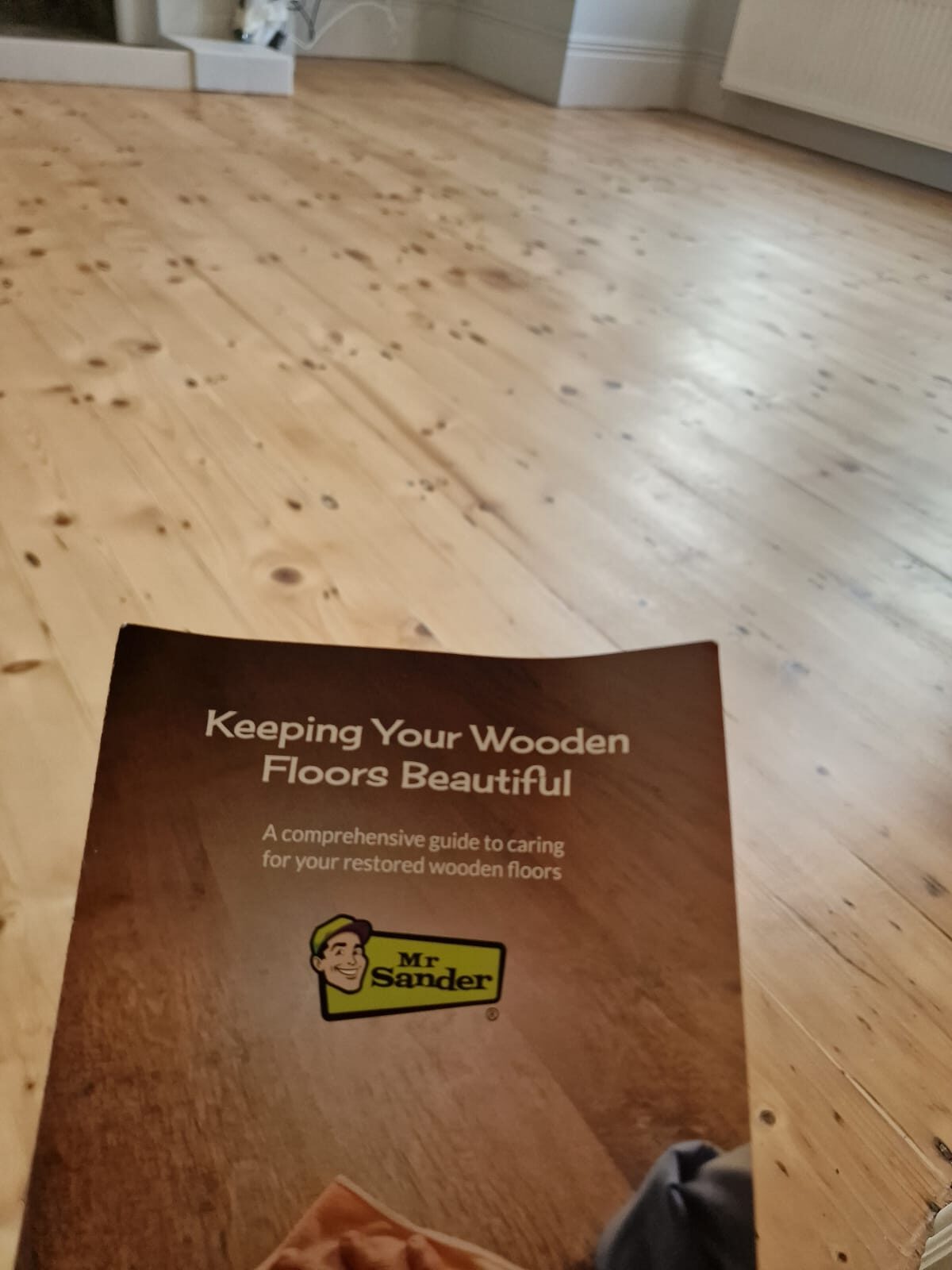 A Mr Sander® brochure titled ‘Keeping Your Wooden Floors Beautiful’ in the foreground, with a freshly sanded and refinished pine floor showcased in the background.