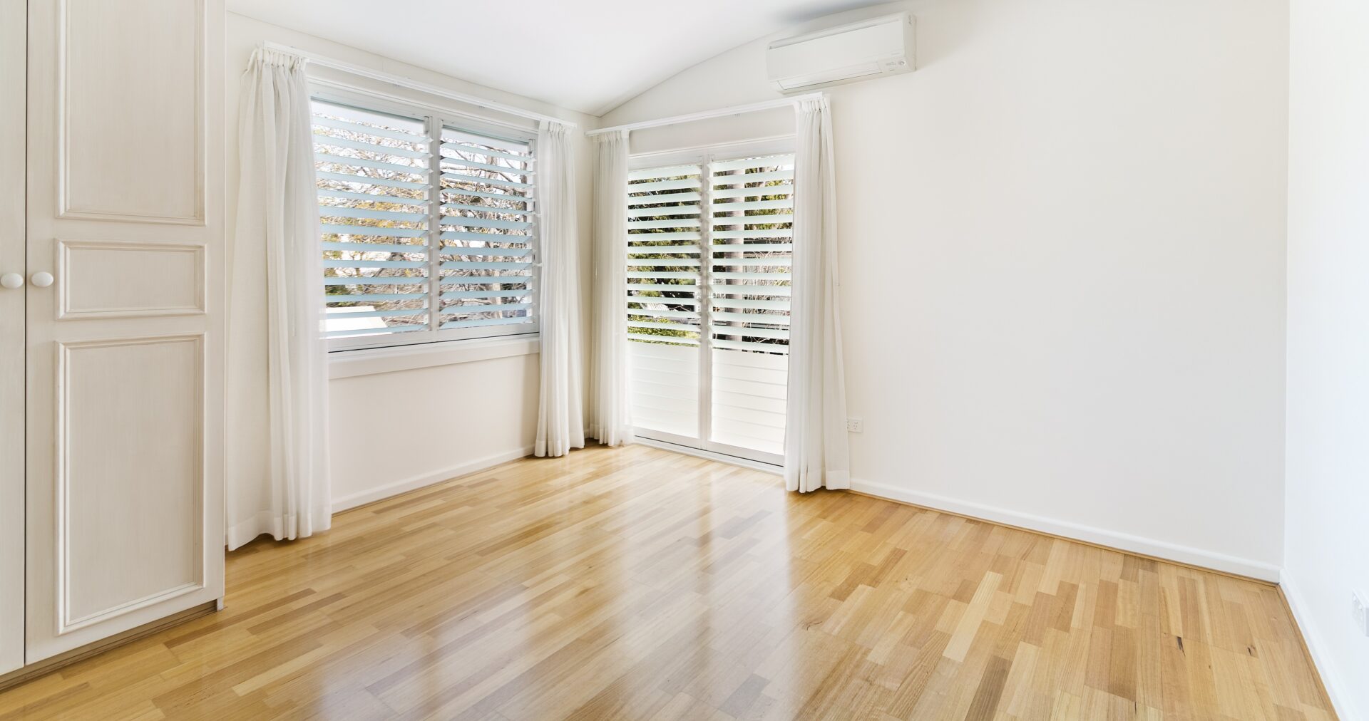Sun-lit bedroom after Floor Sanding and Waxing, showcasing a pale engineered oak plank floor with a silky finish from professional wood floor waxing.
