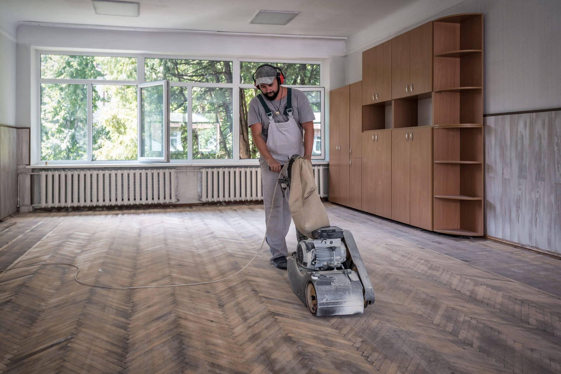 Professional sanding a herringbone parquet floor in an empty rental property with an industrial drum sander