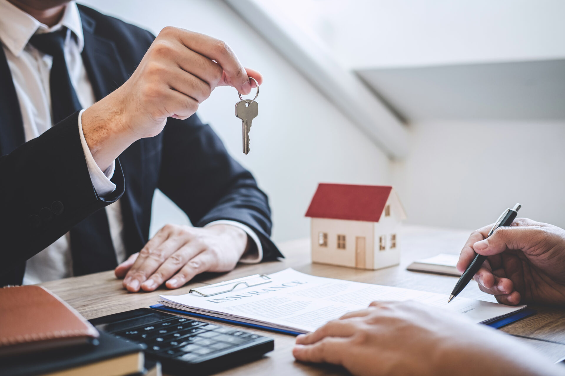 Landlord in suit handing keys to a tenant over tenancy paperwork and a model house, illustrating a successful let after Floor Sanding in Rental Properties