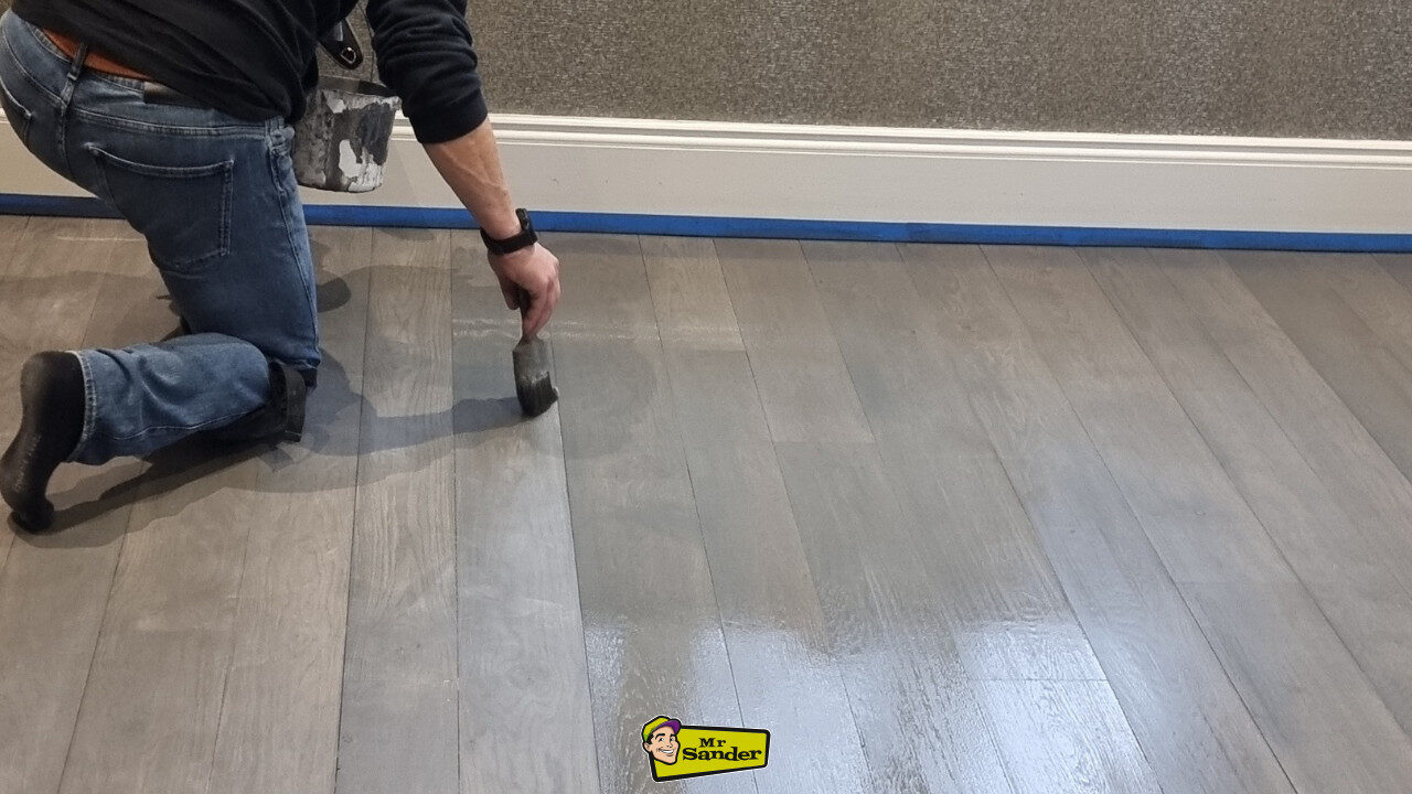A flooring professional applying a grey finish to a newly sanded wooden floor, illustrating how Floor Sanding in Schools and Hospitals creates a polished, hygienic surface.