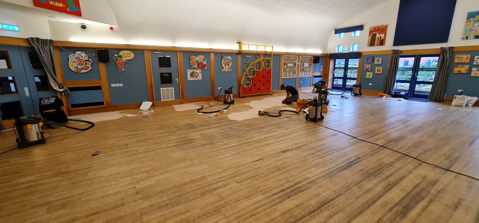 Professional sanding team working on a wooden floor in a UK school hall, demonstrating the need for Floor Sanding in Schools and Hospitals for improved cleanliness and safety.