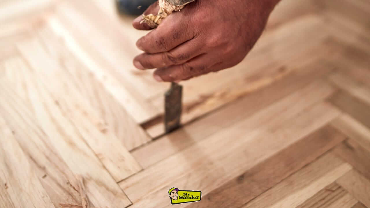 Close-up of a craftsman's hand using a chisel to repair and fit parquet flooring during a restoration project.