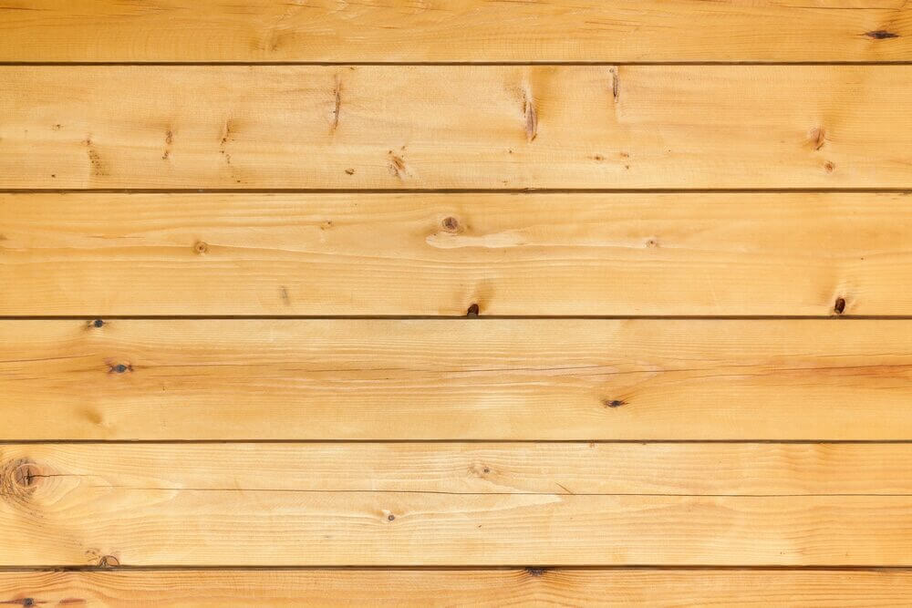 A wooden floor with neatly aligned pine planks, showing smooth surfaces and minimal gaps. The wood has a natural, polished look, highlighting the grain and small knots.