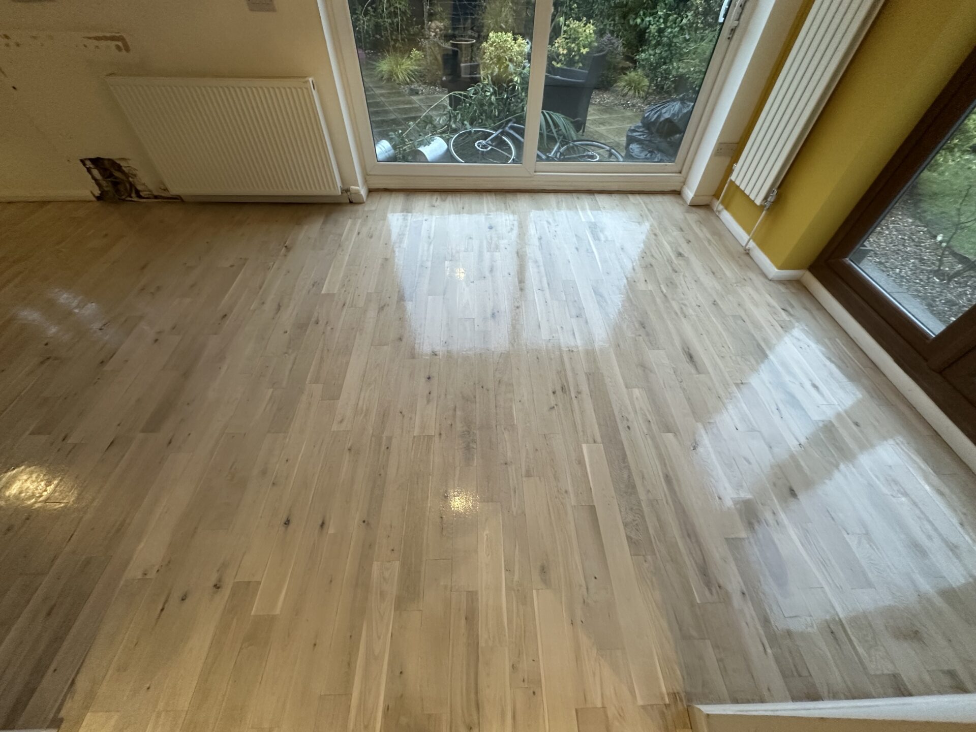 Refinished wood floor with a pale, reflective finish achieved using Bona White Primer, next to a large garden window.