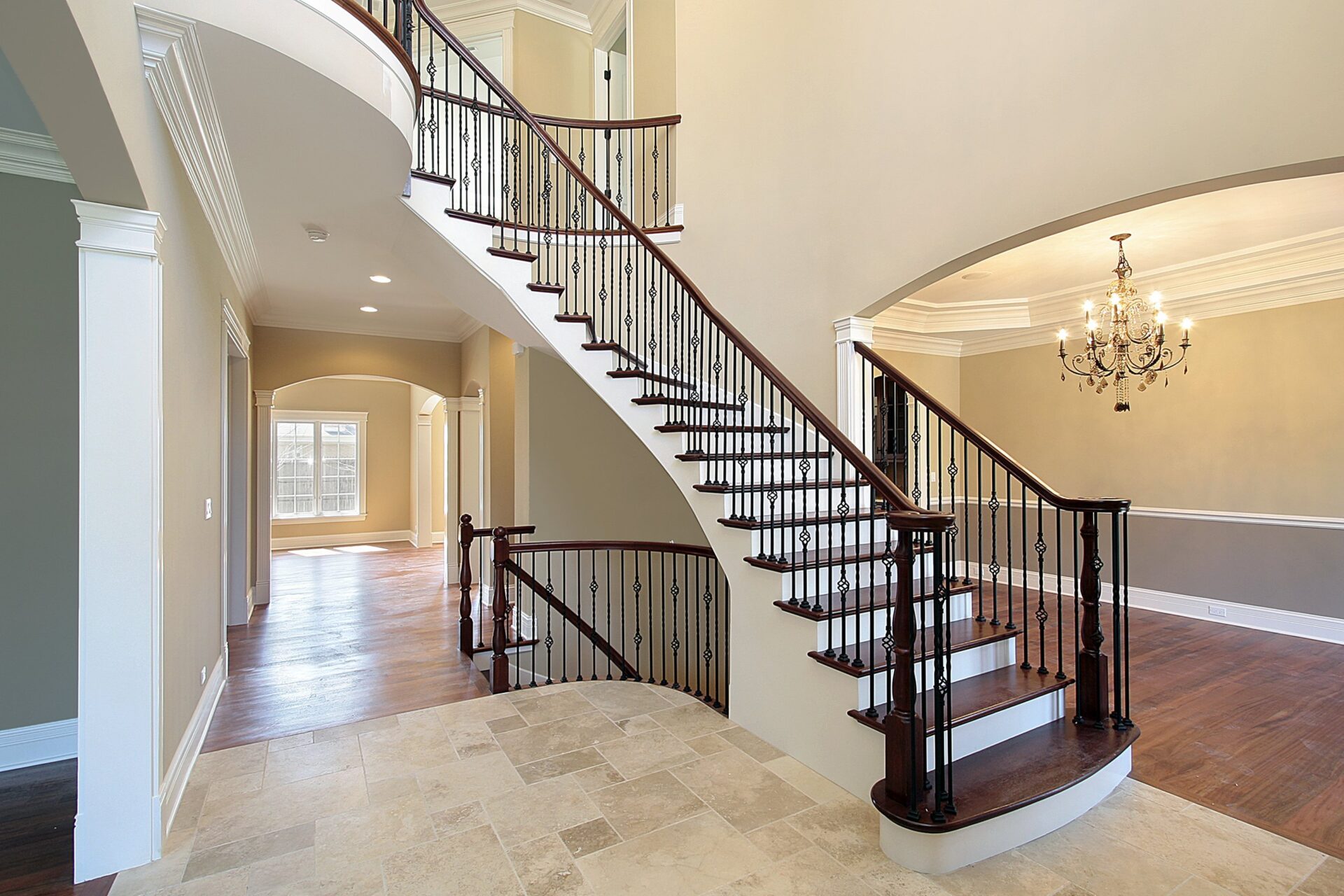 Georgian stair restoration with an elegant curved staircase featuring dark-stained treads, white risers and wrought-iron balustrades beneath a chandelier.
