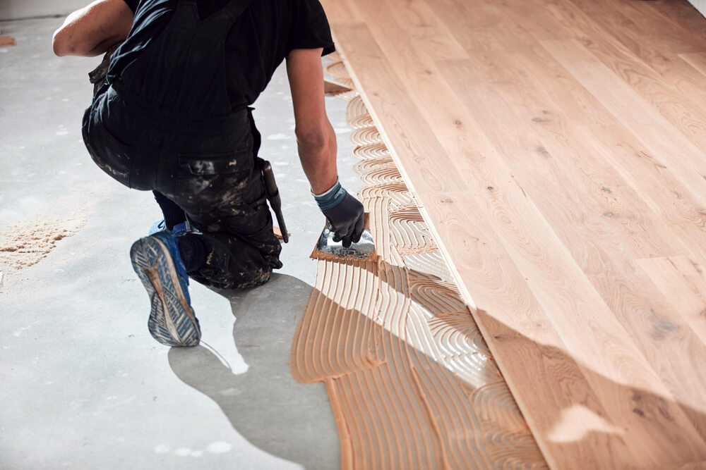 A professional installer carefully applying adhesive on a concrete subfloor and positioning hardwood planks, demonstrating the glue-down wood floor installation method.
