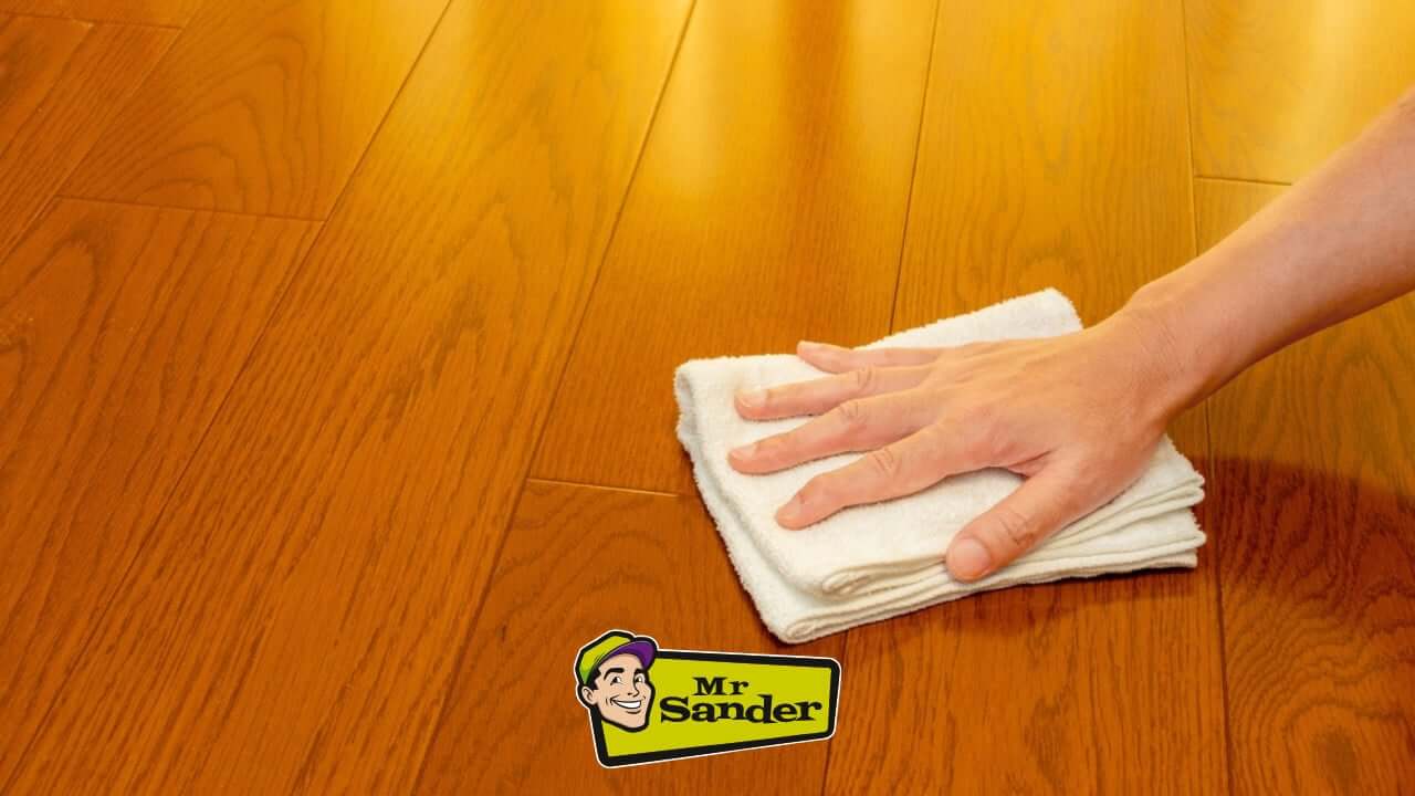 A hand polishing a beautifully refinished hardwood floor using a soft white cloth. The Mr Sander® logo is visible on the image.
