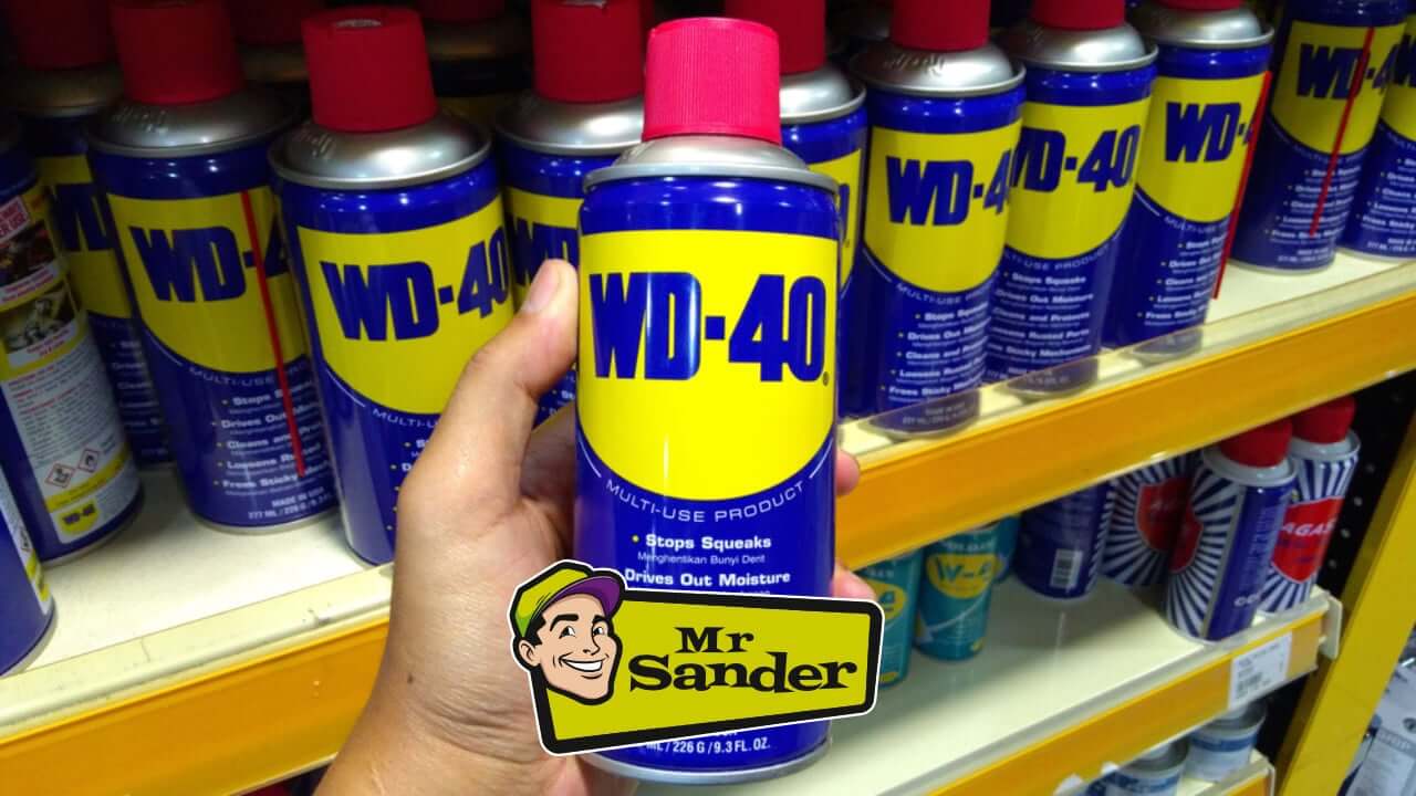 Hand holding a WD-40 can in a store aisle, surrounded by multiple WD-40 products on a shelf, with the Mr Sander® logo placed prominently.