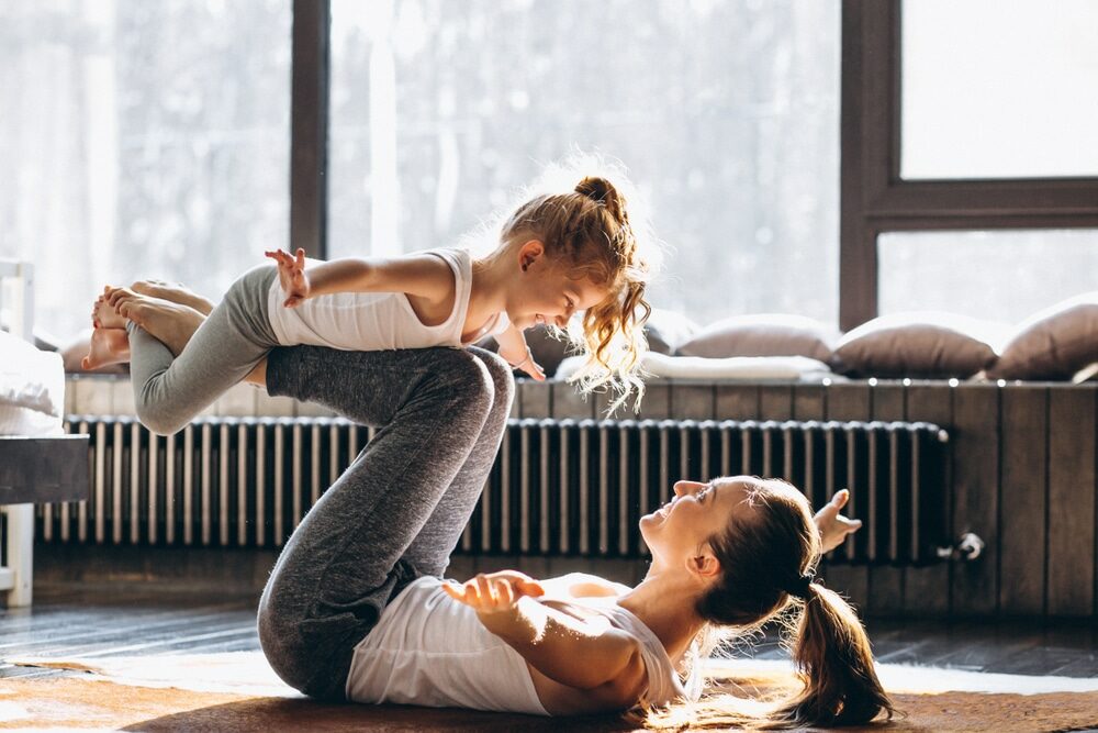 A woman and a young girl practicing yoga together in a sunlit room.