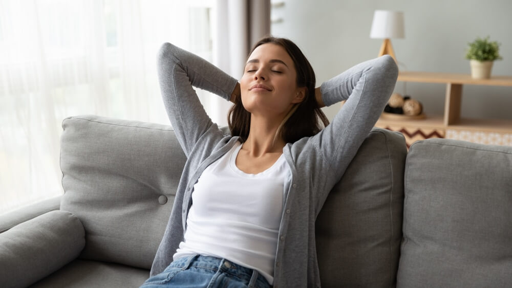 A relaxed woman reclining on a sofa with her hands behind her head, enjoying clean indoor air free of dust and irritants.