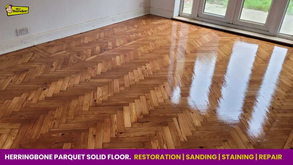 A fully restored herringbone parquet floor with a high-gloss finish, reflecting the nearby windows.
