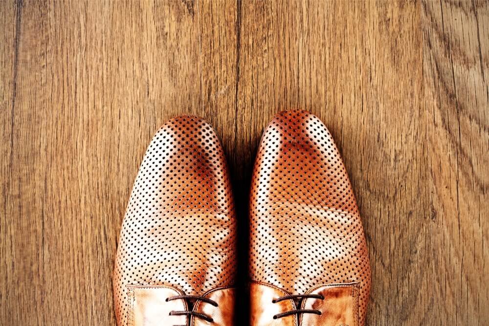 A close-up view of polished leather shoes on a newly refinished wooden floor with a smooth and glossy surface.