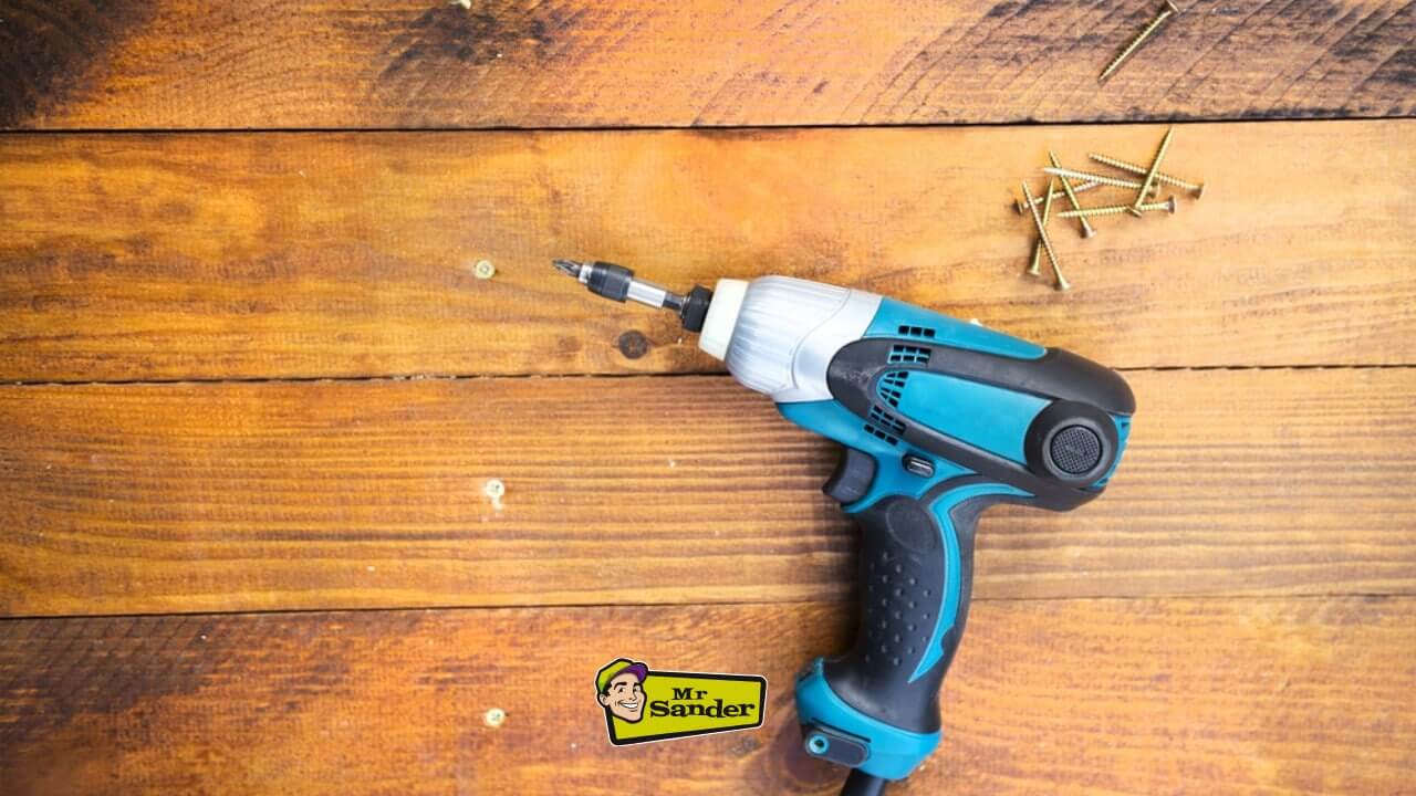 A close-up of a power drill and screws placed on a beautifully refinished wooden floor with a warm, natural finish.