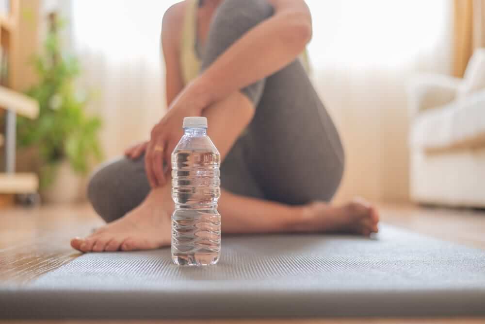 A woman sitting on a yoga mat with a water bottle in front of her, highlighting how hydration and exercise can support lung health.