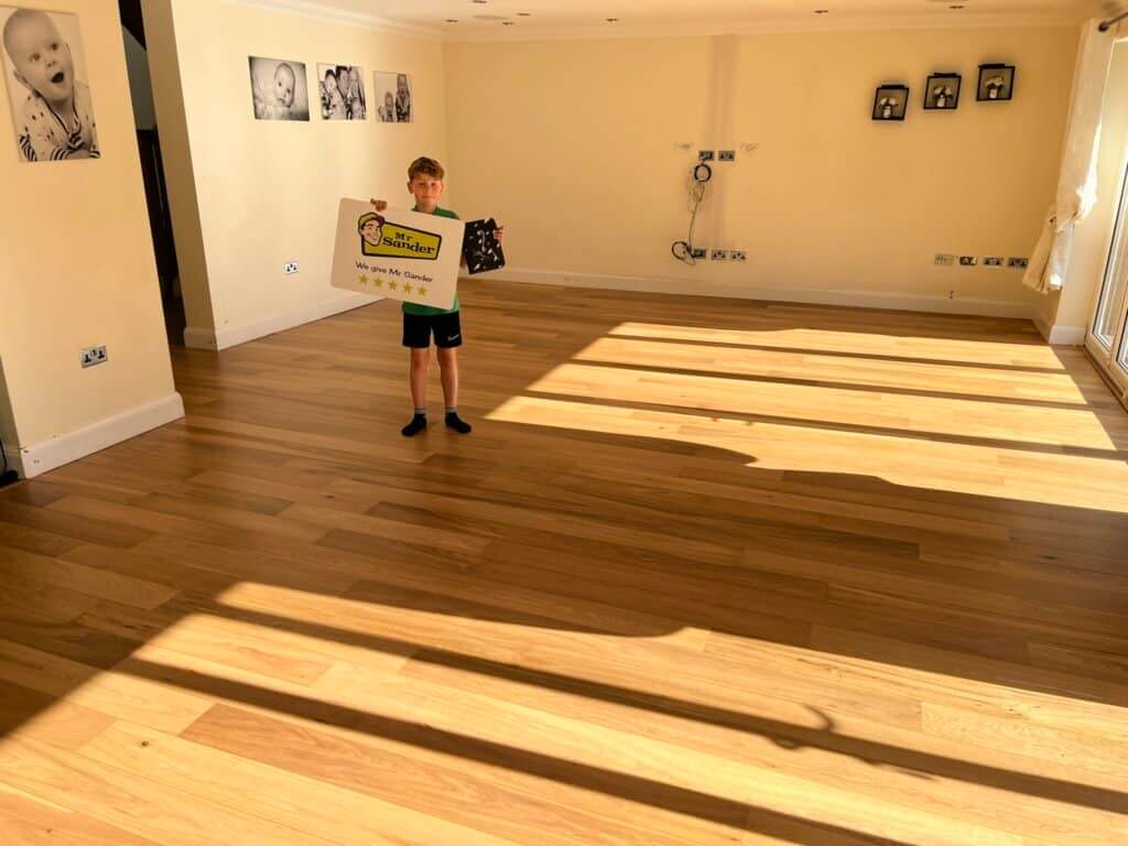 Child holding a Mr Sander® sign standing in a large living room with newly sanded and refinished wooden floor