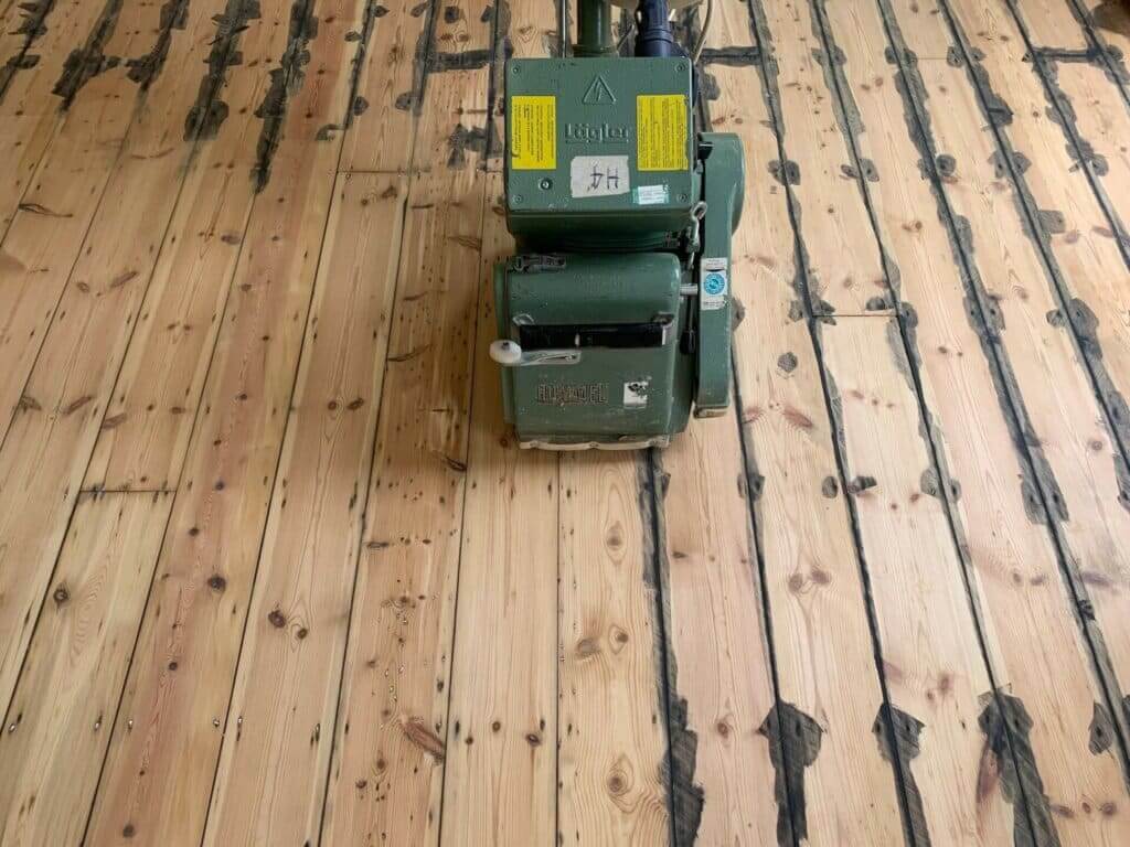 Mr Sander® using Lagler HUMMEL® to sand pine floor in, UK living room. Specifications: 2.2 kW single-phase AC motor, 230V, 50Hz, thermal overload protection, 200mm sanding drum width, 2400 rpm drum speed, 200x750mm sanding belt size, 79kg weight. Features: high powered sanding, low dust emissions, quick belt change, 30+ years lifespan, 3x adjustable pressure, LED work light upgrade available.