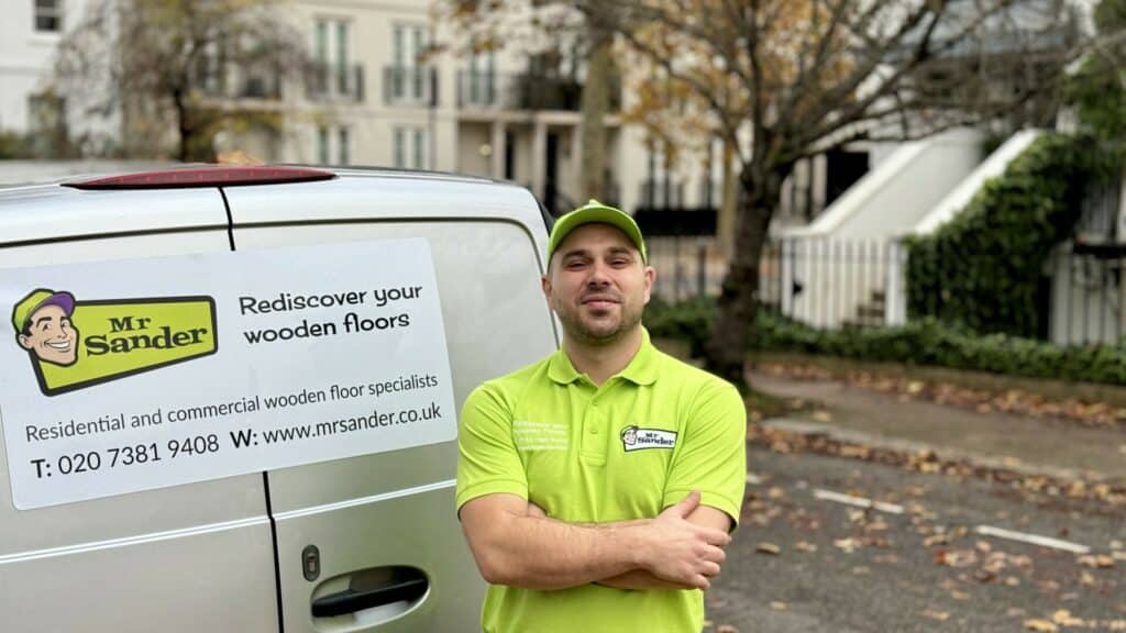 Mr. Sander® employee standing in front of a company van with signage advertising wooden floor services.