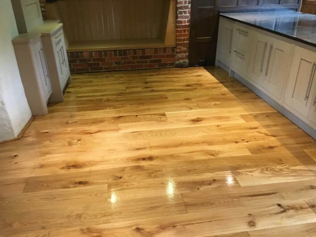 Beautifully refinished wooden floor in a kitchen with white cabinets and exposed brick wall.