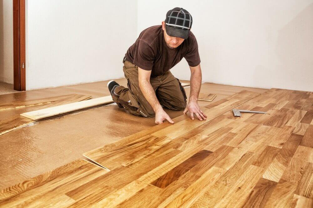 A professional installer kneels on newly laid hardwood boards, carefully positioning them for a perfect finish during Kahrs and Junckers floor fitting.