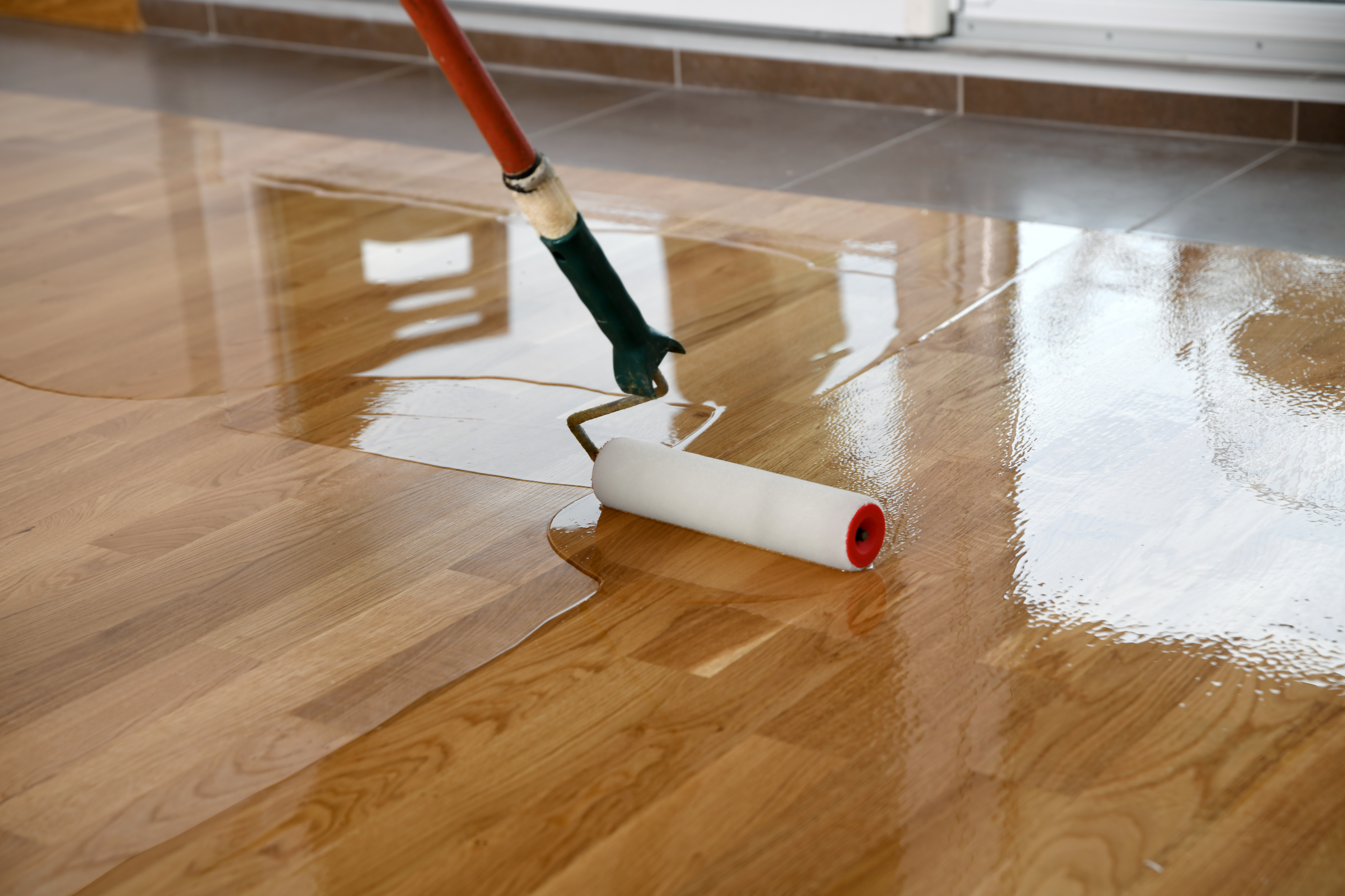 A worker is using a 225mm short pile roller to apply a lacquer coating to wooden floors.