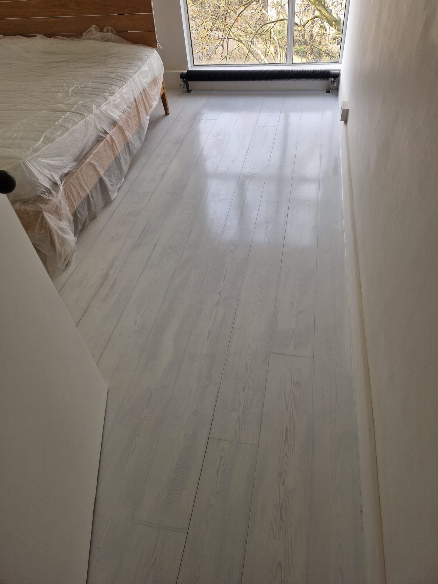 Colourful Hardwax Oils in a light grey wash brightening freshly sanded bedroom floorboards beneath a large window.