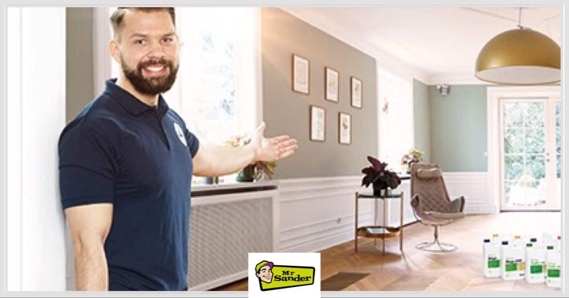 A Mr Sander professional gesturing towards a newly refinished parquet floor in a bright living room, illustrating how low-VOC finishes benefit allergy sufferers and sensitive occupants.