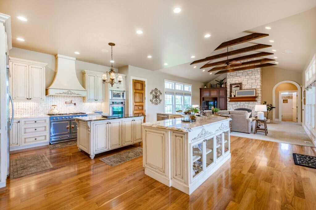 Open-concept kitchen and living area showcasing the Beauty of Natural hardwood floors, cream cabinetry, ornate stove, and a stone fireplace.