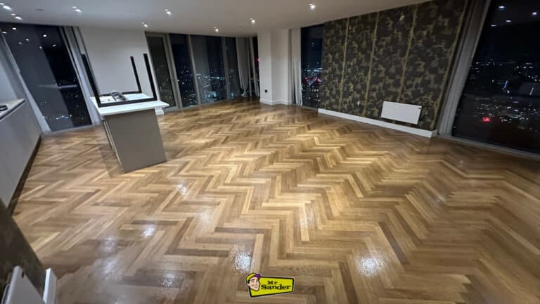 A luxurious herringbone oak parquet floor fully restored by Mr. Sander, showcasing a high-gloss finish in a modern interior with cityscape views.