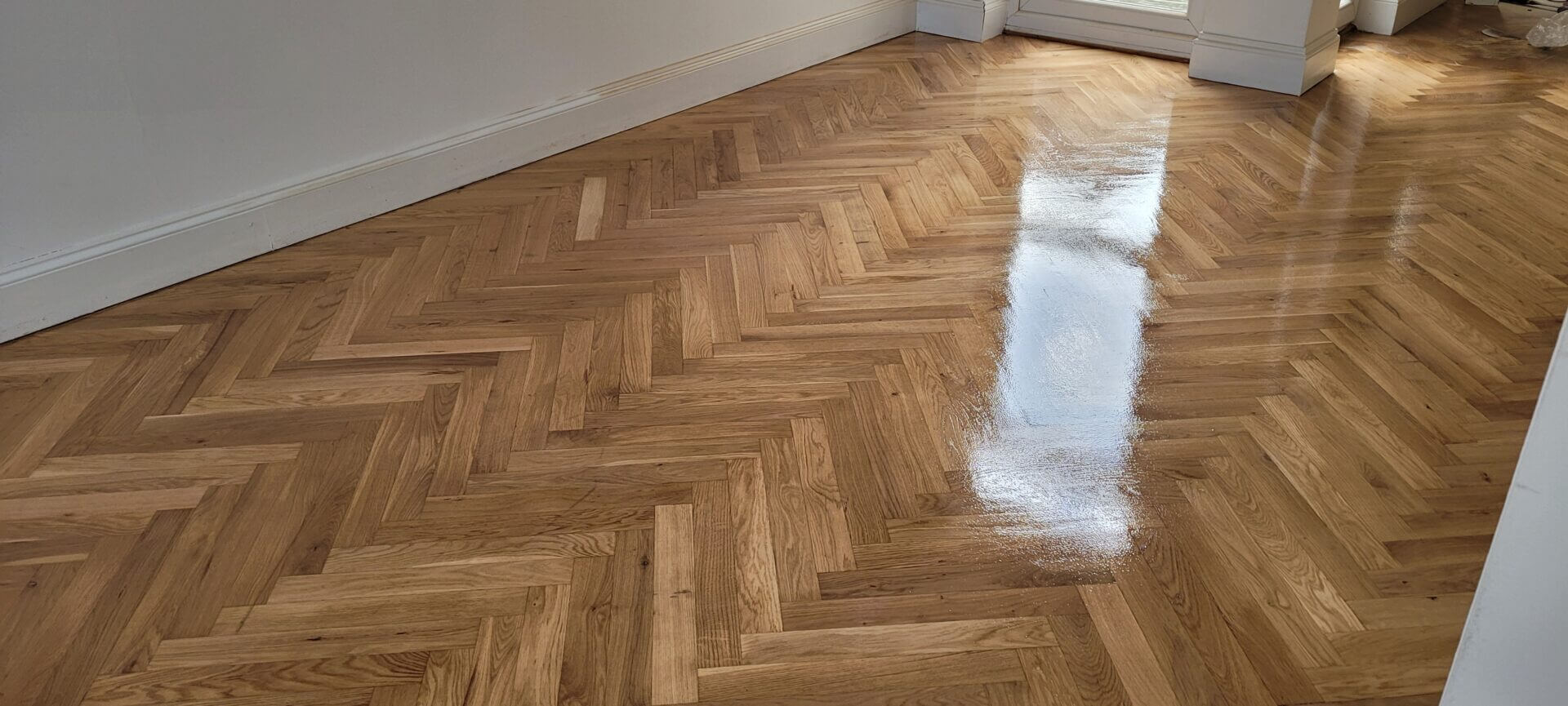 A newly laid and polished herringbone parquet floor with a glossy reflection, showcasing expert North London Floor Fitting results.