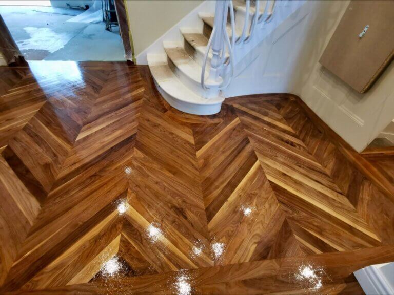 A newly installed, high-gloss walnut chevron parquet floor near a curved staircase, demonstrating premium North London Floor Fitting craftsmanship.