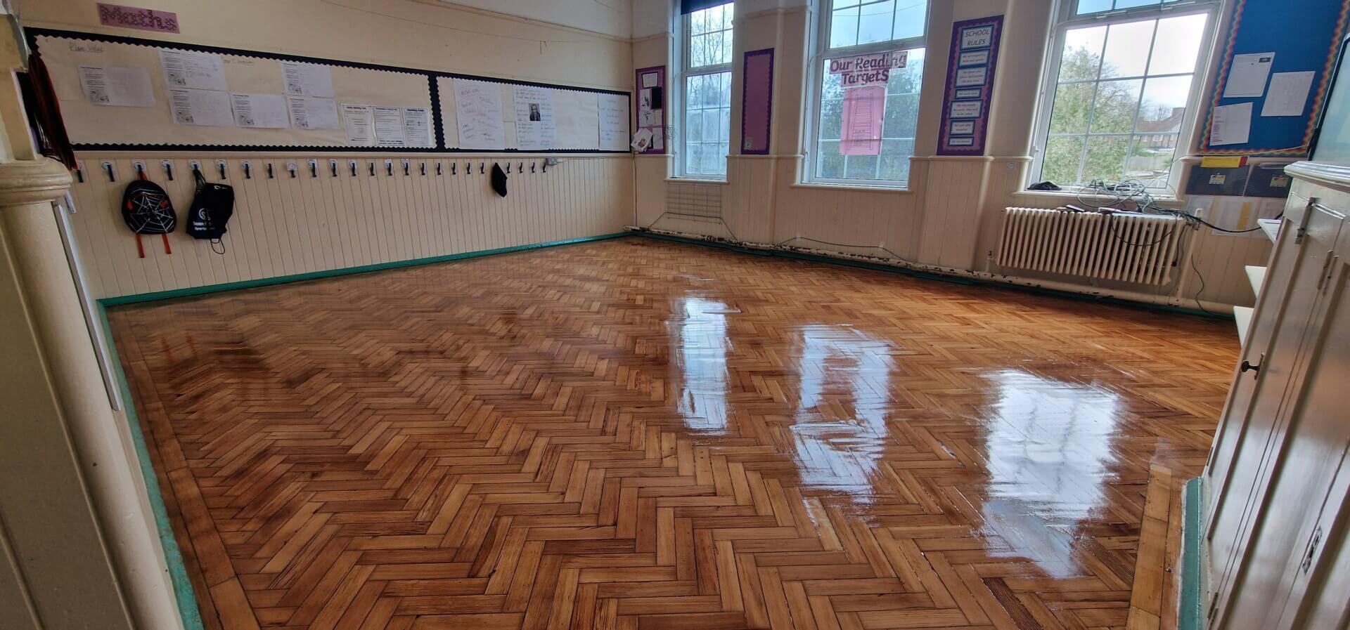 A UK school classroom showcasing a newly refinished herringbone parquet wood floor with a high-gloss finish achieved through Overnight Floor Sanding.