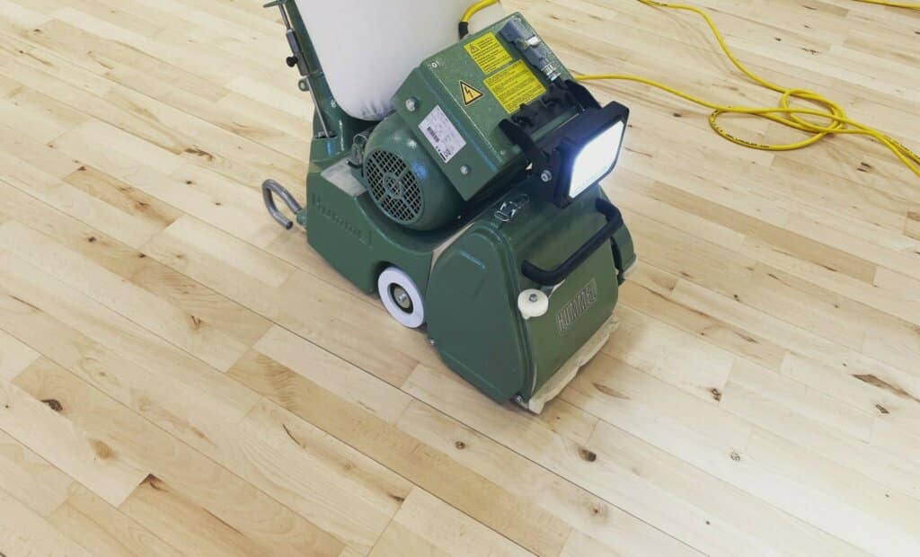 Mr Sander® is sanding an oak floor in a living room in Harold Wood, UK, using the Lagler HUMMEL. This machine features a powerful LED lighting system, ideal for finishing both large and small areas, with high powered aggressive sanding, low dust emissions, and easy belt changes. The technical specs include a single-phase AC motor with 230 V / 50 CPS / 2.2 kW & thermal overload protection, a sanding drum width of 200 mm, drum speed of 2400 rpm, sanding belt dimensions of 200 x 750 mm, and a total machine weight of 79 kg.