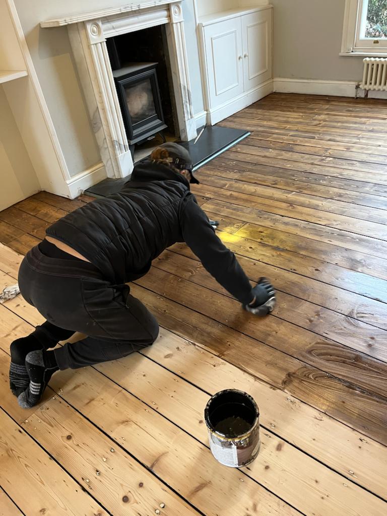 A person applying finish to a wooden floor near a fireplace