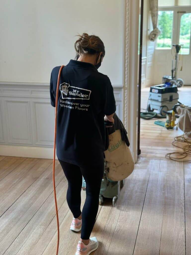 A girl from Mr Sander® is sanding an oak plank floor in a living room in Elephant & Castle, UK, using the Lagler HUMMEL. The HUMMEL features a powerful LED lighting system, high powered aggressive sanding, and extremely low dust emissions. It has a single-phase AC motor with 230 V / 50 CPS / 2.2 kW & thermal overload protection, a sanding drum width of 200 mm, drum speed of 2400 rpm, sanding belt dimensions of 200 x 750 mm, and a machine weight of 79 kg.