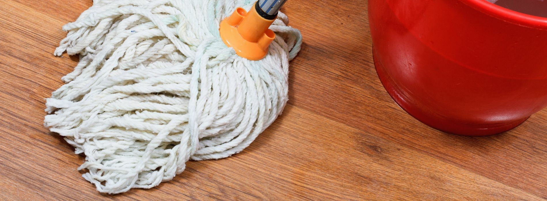 A mop and a red cup on a wooden floor.