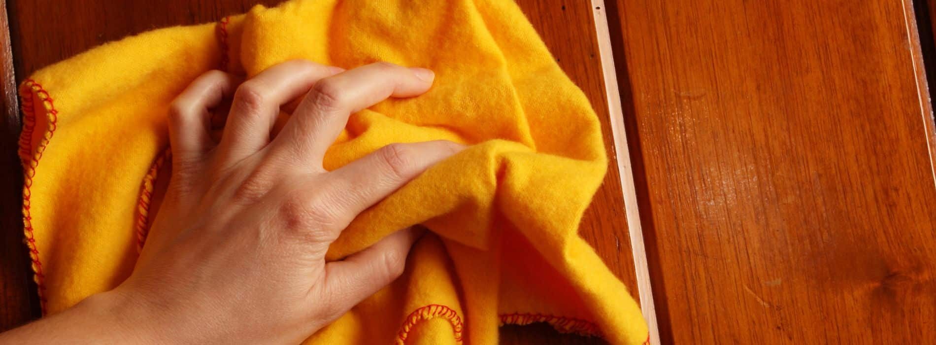 A person's hand is on a yellow towel on the wooden floor.