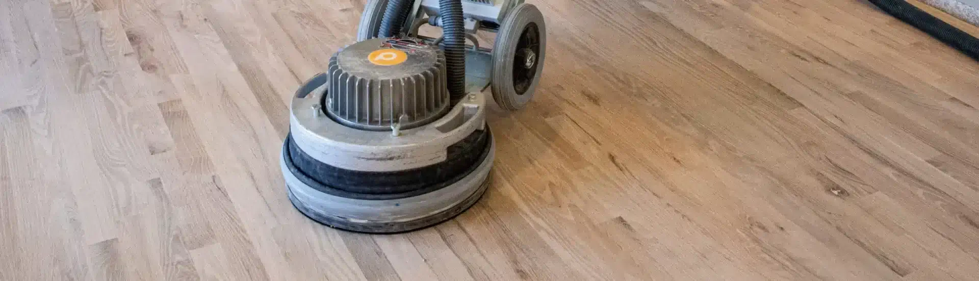 A man from Mr Sander® is using a PALLMANN SPIDER wood floor sanding machine on an oak floor in a living room in Crossness, UK. The PALLMANN SPIDER features 360° illumination, switchable power reserve, and triple-disc technology. It operates with a power supply of 230 V, power consumption of 2000 W, rotation speed of 50-400 RPM, weight of 42 kg, sanding width of 400 mm, and additional weight of 15 kg.