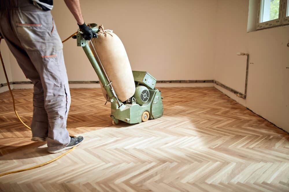 A person using a professional floor sanding machine on herringbone parquet flooring.