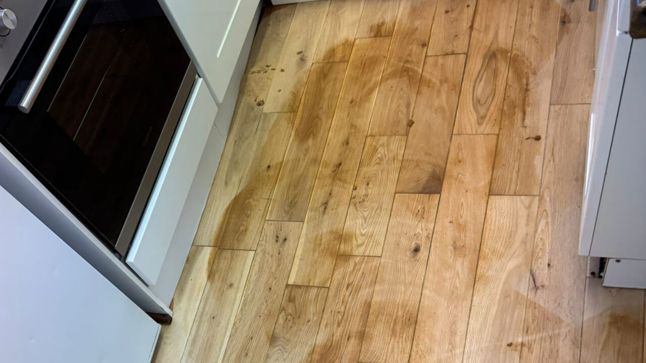 A kitchen floor with blotchy patches and uneven staining, showing the problematic results of skipping floor sanding before applying a new finish.