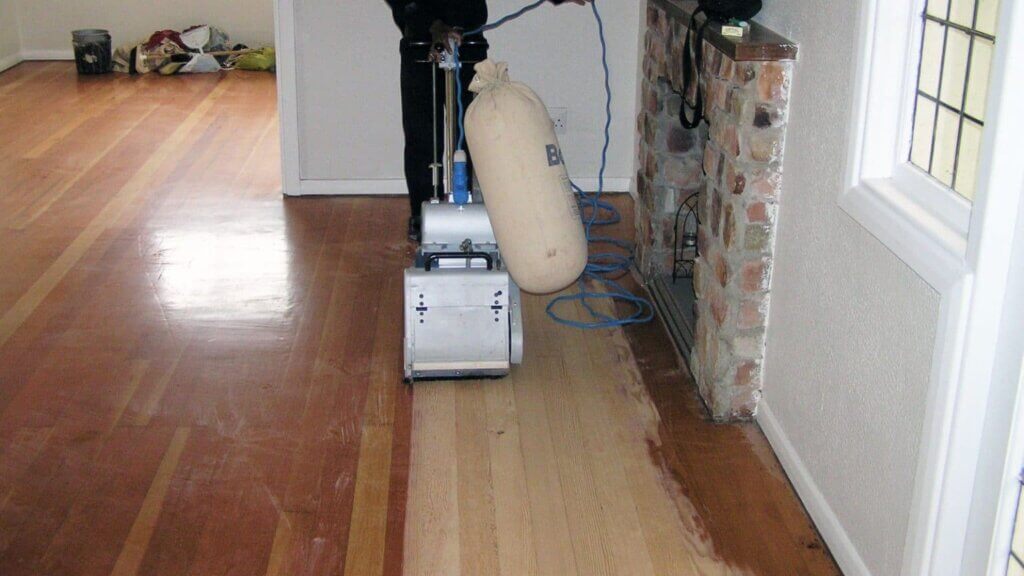 A man from Mr Sander® is using a Bona Belt (AMO110001.3) sander to refinish a wooden floor in Peckham. The machine features a 2.2 kW motor, 1-phase power, 200x750 mm and 250x750 mm sanding belt options, 200 mm and 250 mm drum widths, and weighs 74 kg.