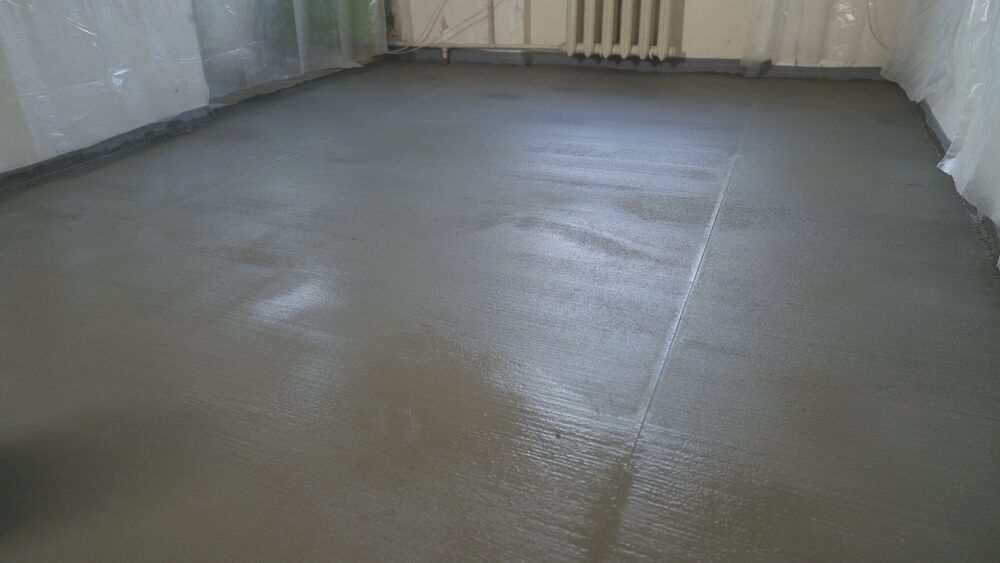 A freshly poured, smooth concrete subfloor curing in a room, providing a stable foundation for upcoming floor installation.