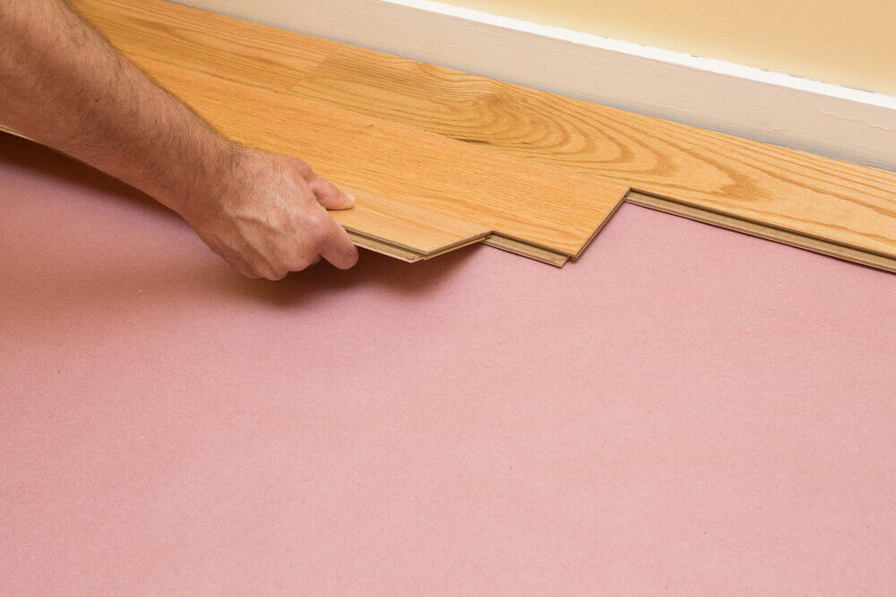 Close-up of a hand positioning oak boards during a Hardwood Floor Fitting installation over an underlay.