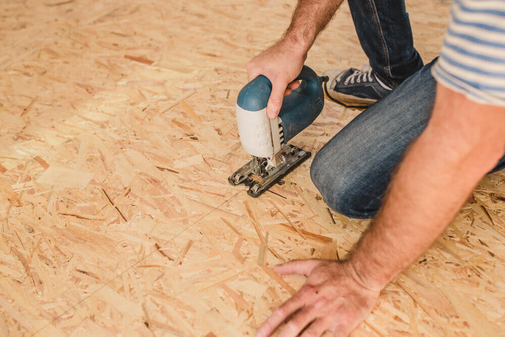 A flooring professional uses a jigsaw to cut an OSB panel, ensuring a precise fit for a stable subfloor.