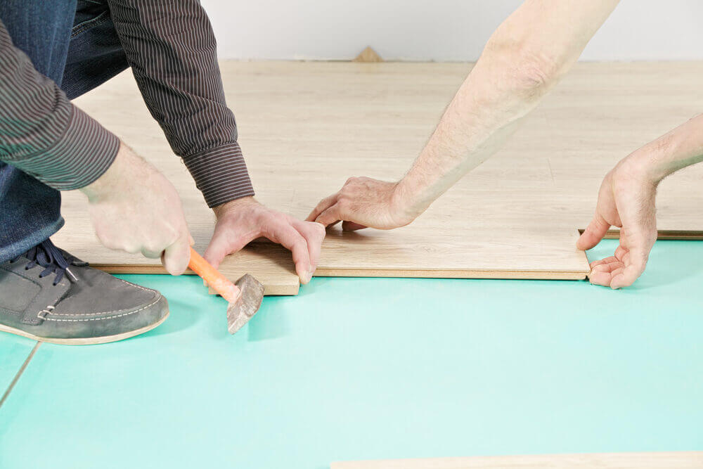 Two floor fitters carefully locking wood planks over a green underlay, ensuring a tight, professional fit for a floating floor installation.