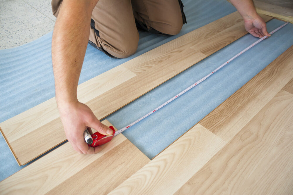 Installer measuring laminate planks for a floating floors installation.