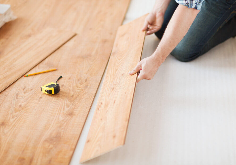 Homeowner positioning an engineered wood plank with a measuring tape close at hand during a South London floor fitting.
